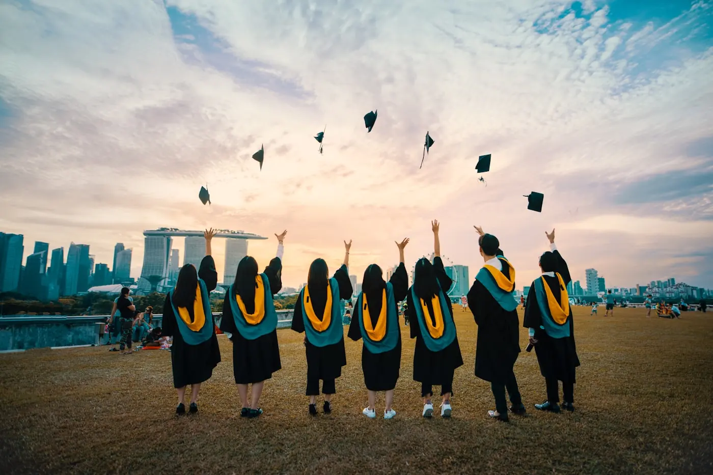 Graduating students throwing their caps into the air against a sunset skyline